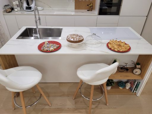 Piano cucina moderna con due sgabelli, dolci su piatti rossi e decorazioni.
