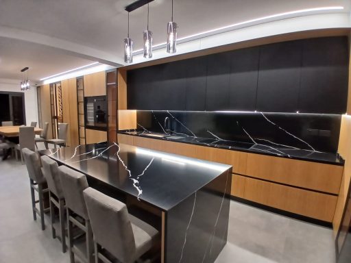 Modern kitchen with sleek black countertops, wooden cabinetry, and stylish pendant lights.